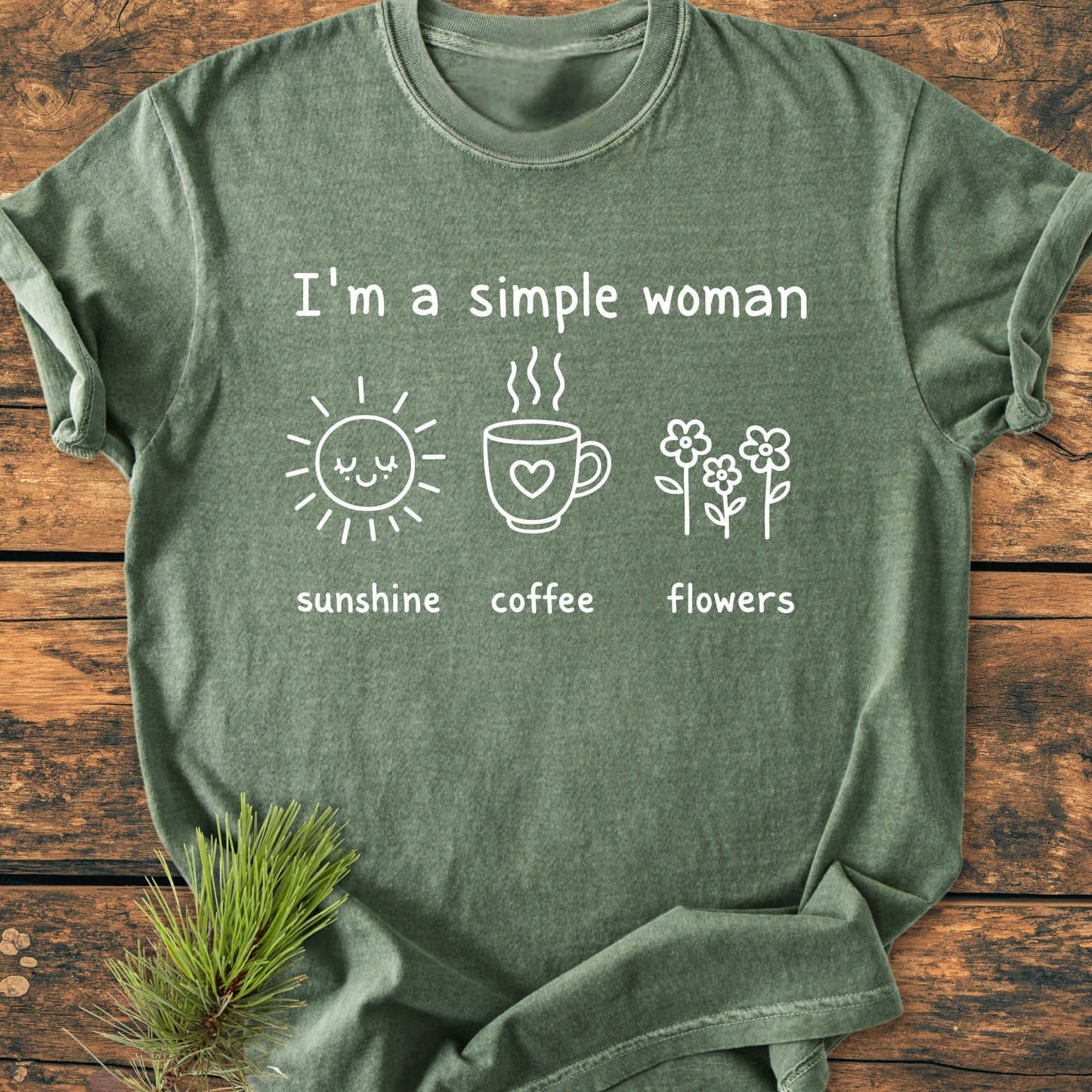 I'm A Simple Woman. Sunshine Coffee Flowers - Vintage Wash Tee displayed flat with white line-art icons and text, resting on a wooden surface, adorned with a small evergreen sprig in one corner.