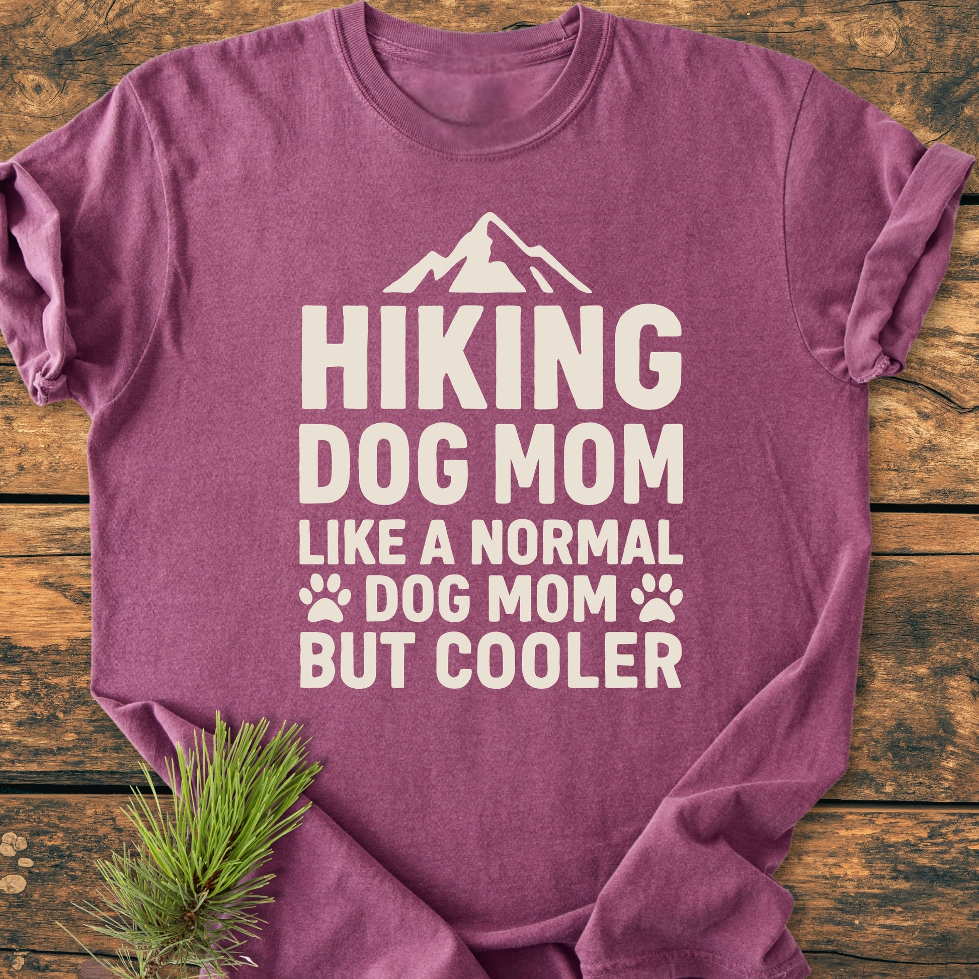 Hiking Dog Mom - Vintage Wash Tee, folded on wood, showcases an off-white slogan with mountain and paw icons. Made from soft, ring-spun cotton, it offers a relaxed fit and durable stitching.