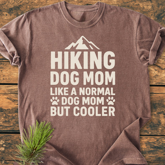 Hiking Dog Mom - Vintage Wash Tee featuring a mountain graphic and playful slogan, displayed flat on wood with pine sprig accent; crafted from soft, durable, pre-shrunk ring-spun cotton.