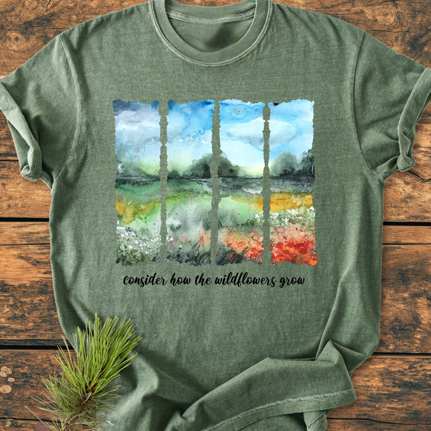 Consider How The Wildflowers Grow - Vintage Heavyweight Tee features a watercolor-style landscape with wildflowers. Laid on rustic wood, it's styled with a pine branch, showcasing its relaxed, durable design.