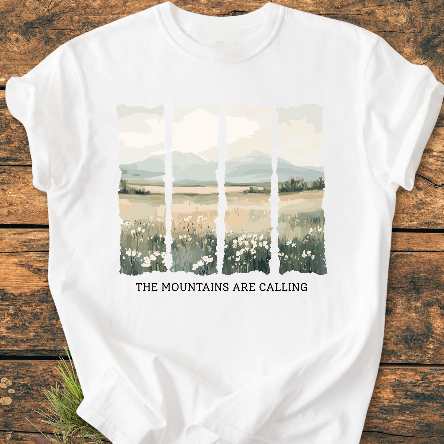 The Mountains Are Calling - Vintage Heavyweight Tee features a stylized landscape graphic in five vertical panels with wildflowers, plains, and mountains, beneath which the phrase is printed on a soft white t-shirt.