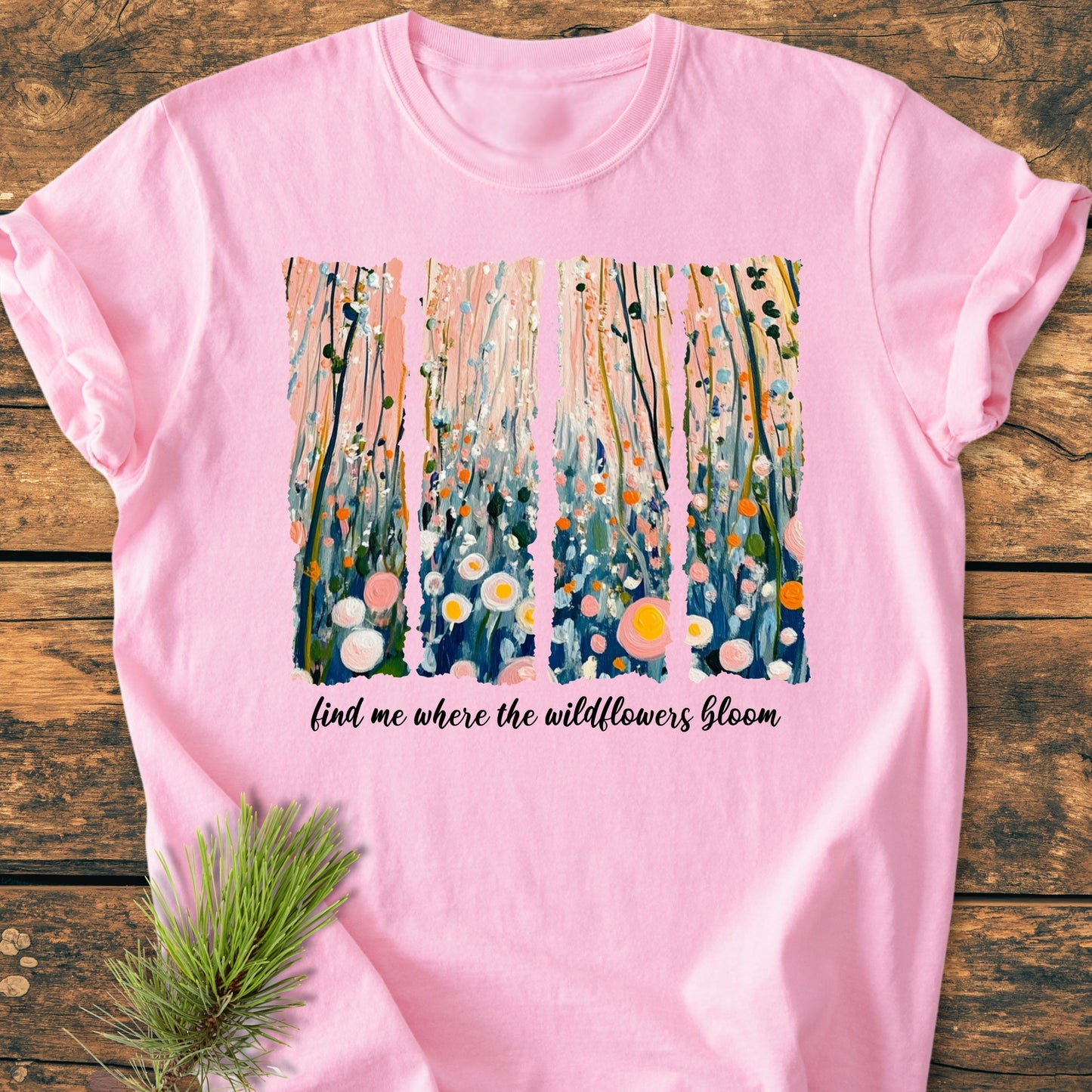 Find Me Where The Wildflowers Bloom - Vintage Heavyweight Tee features four vertical pastel wildflower panels and a scripted phrase on a soft pink T-shirt, styled with a pine branch on rustic wood.
