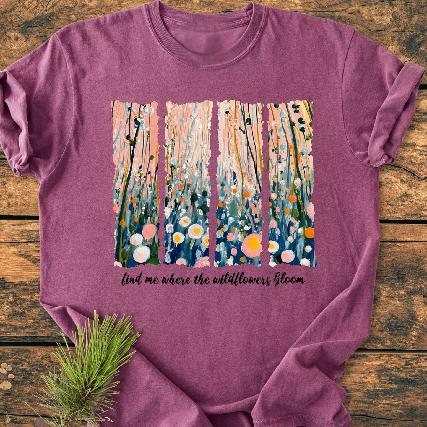 Find Me Where The Wildflowers Bloom - Vintage Heavyweight Tee features a heather-purple hue with a wildflower graphic and motto on the chest, laid flat on a wooden surface.