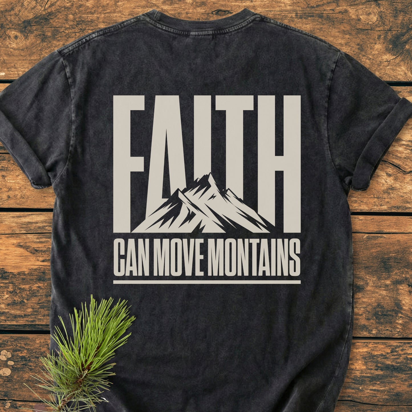 Faith Moves Mountains BACK PRINT - Vintage Wash Tee featuring 'FAITH' and mountain silhouette on back. Laid flat with pine sprig accent, showcasing its relaxed fit and durable, soft-washed cotton fabric.