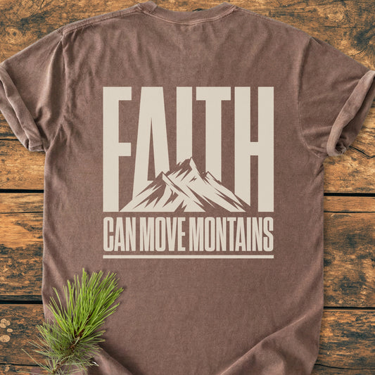 Faith Moves Mountains BACK PRINT - Vintage Wash Tee featuring a brown, crew-neck design with FAITH and CAN MOVE MOUNTAINS in cream letters, laid on a wooden surface with pine needles.