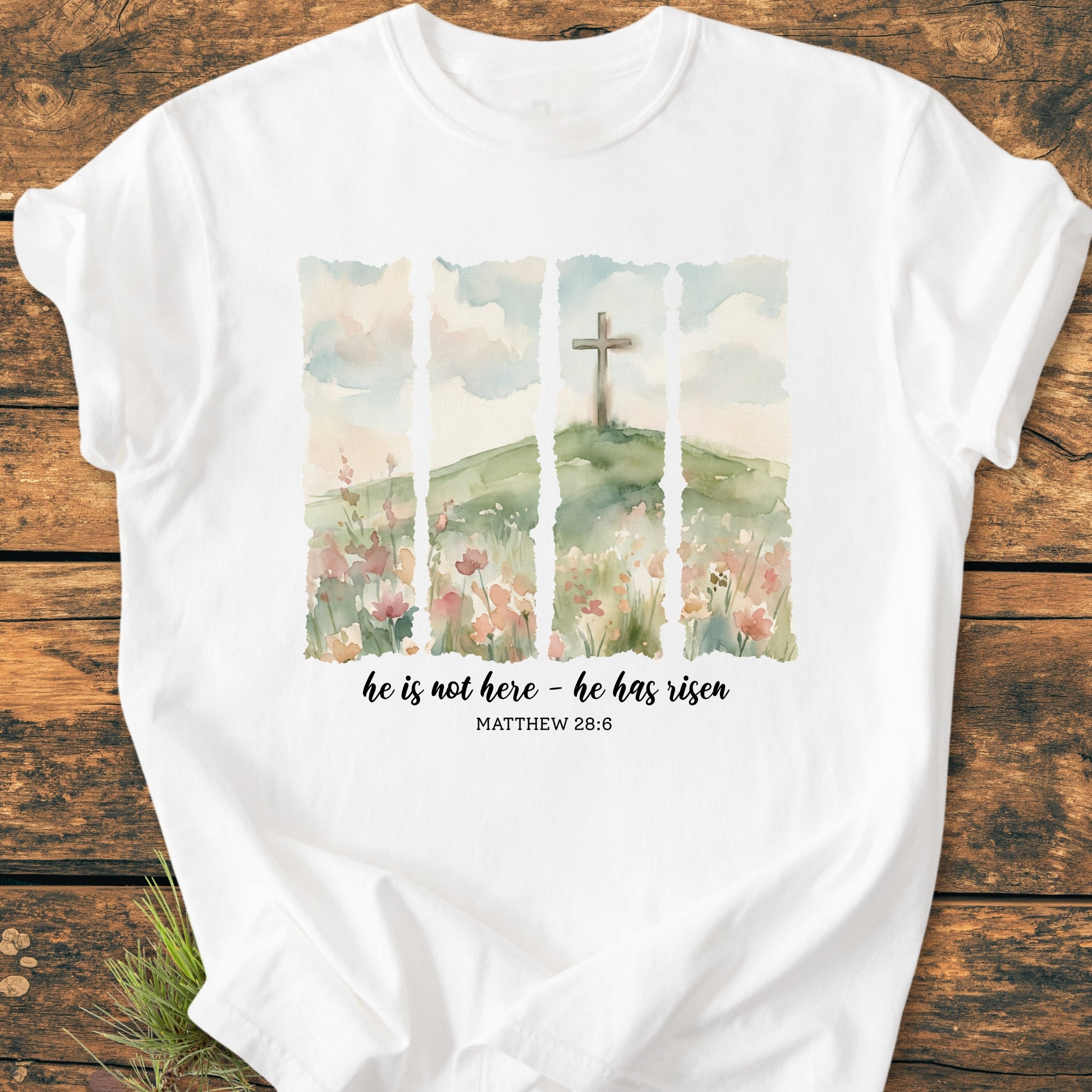He Is Not Here. He Has Risen - Vintage Heavyweight Tee featuring a watercolor-style illustration of a grassy hill with a cross and floral accents, accompanied by Matthew 28:6 scripture on a white garment-dyed T-shirt.