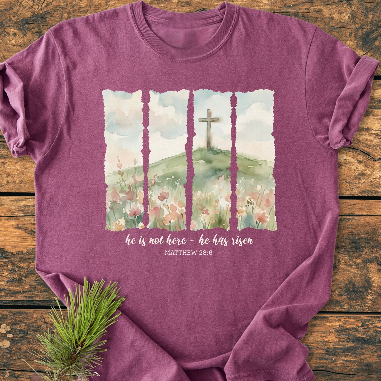 He Is Not Here. He Has Risen - Vintage Heavyweight Tee features a four-panel watercolor scene of a cross on a hill with Scripture, displayed on a heather-purple T-shirt styled with a pine sprig.