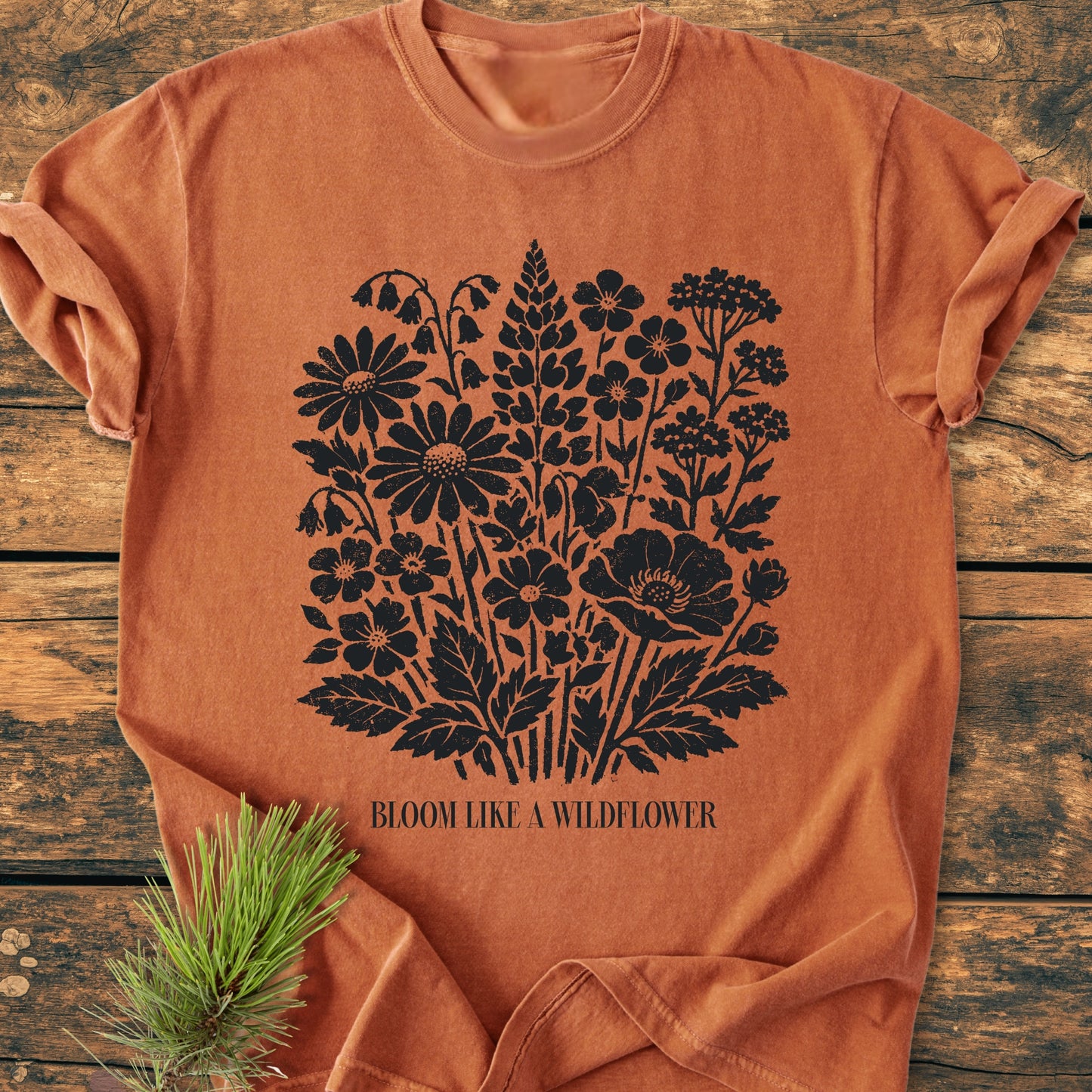 Bloom Like A Wildflower - Vintage Heavyweight Tee: Rust-orange crew-neck with black wildflower bouquet graphic and slogan, styled with a pine sprig on a wooden surface. Cozy, durable, pre-shrunk.