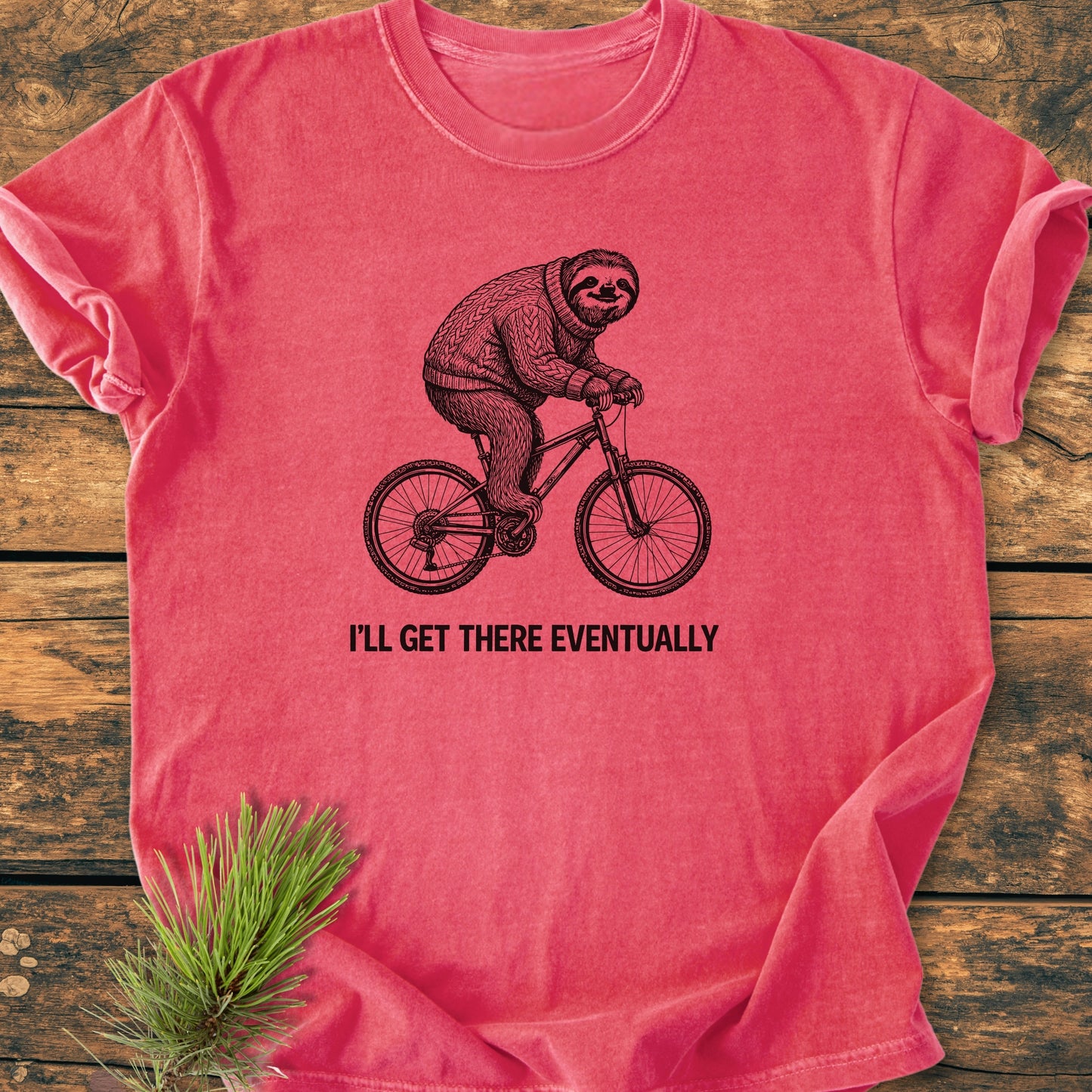 I'll Get There Eventually - Vintage Wash Tee featuring a sloth in a knit sweater on a bicycle, laid on wood, with a conifer sprig. Made from soft, pre-shrunk, 100% ring-spun cotton.