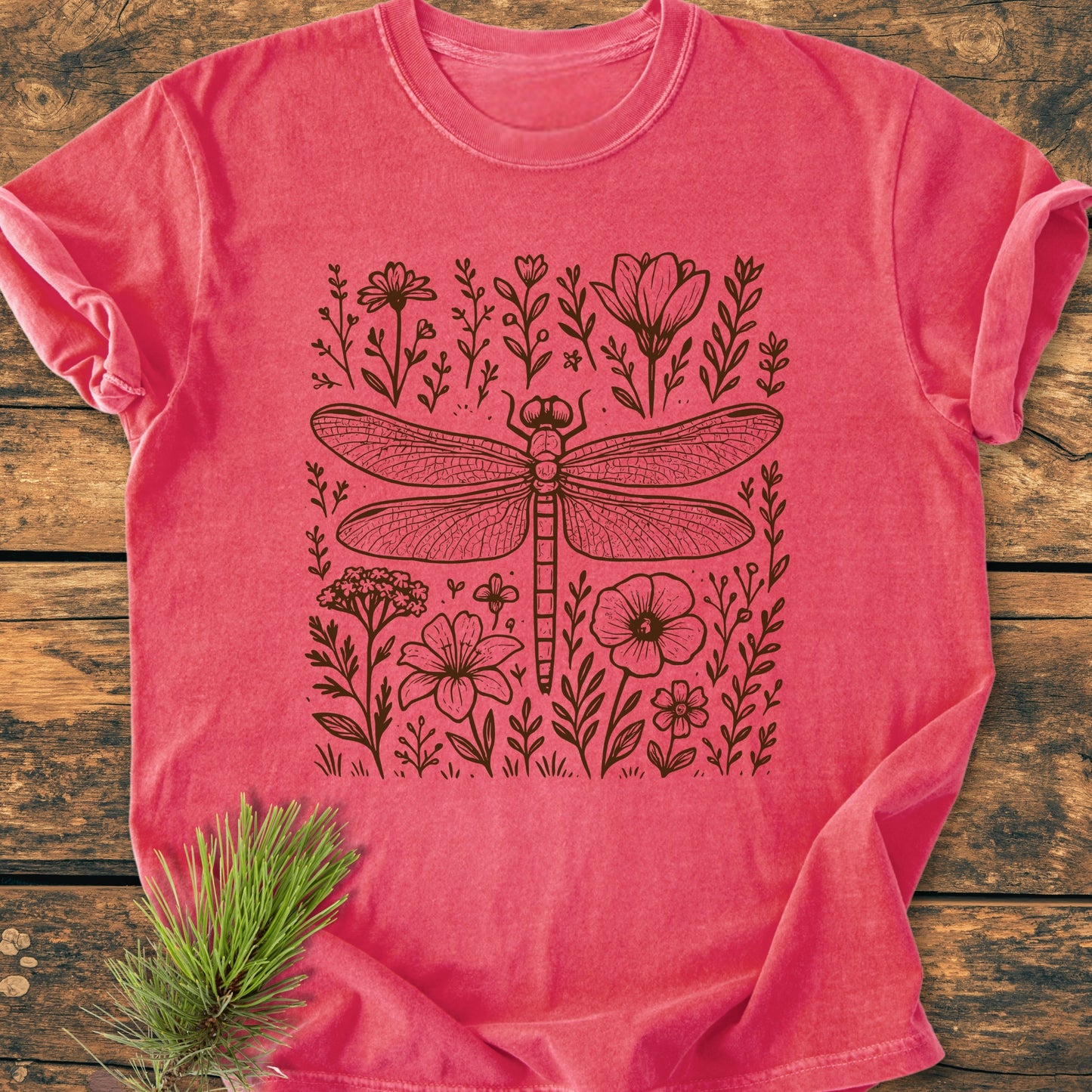 Dragonfly - Vintage Heavyweight Tee featuring a black line-art dragonfly and wildflowers design, displayed on a wooden surface with a pine sprig beside it. Made from soft, durable, 100% ring-spun cotton.