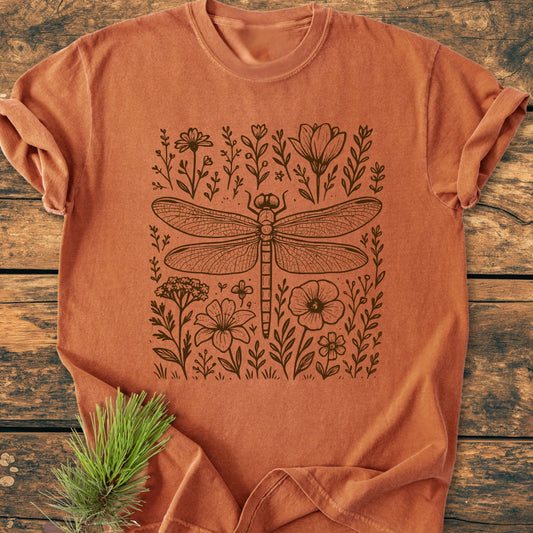 Dragonfly - Vintage Heavyweight Tee features a dragonfly and wildflowers design on a rust-orange, short-sleeved shirt, laid on wood, highlighting its relaxed fit and garment-dyed softness.