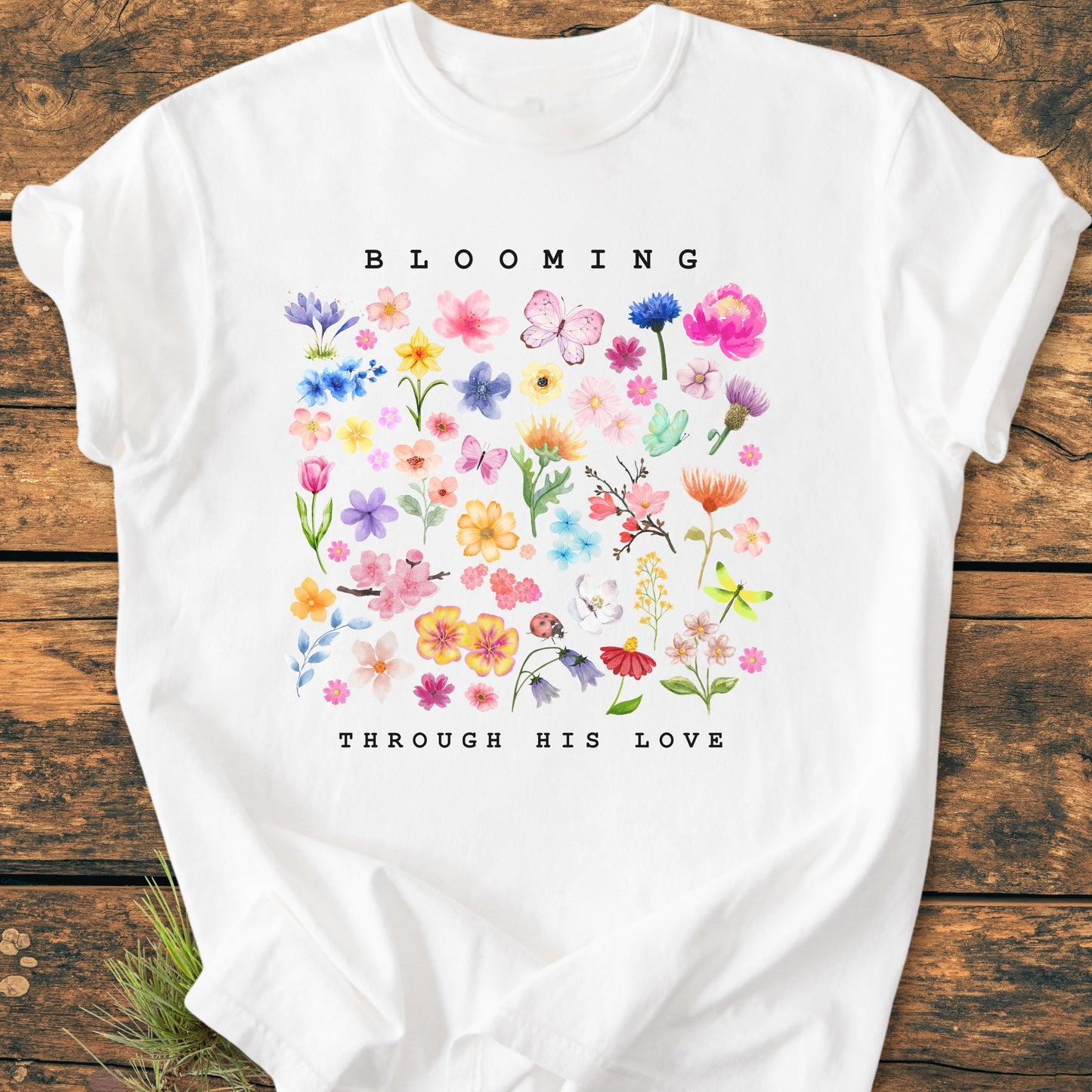 Blooming Through His Love - Vintage Wash Tee features a grid of watercolor-style blooms and insects with text above and below on a soft, ring-spun cotton T-shirt, laid flat.