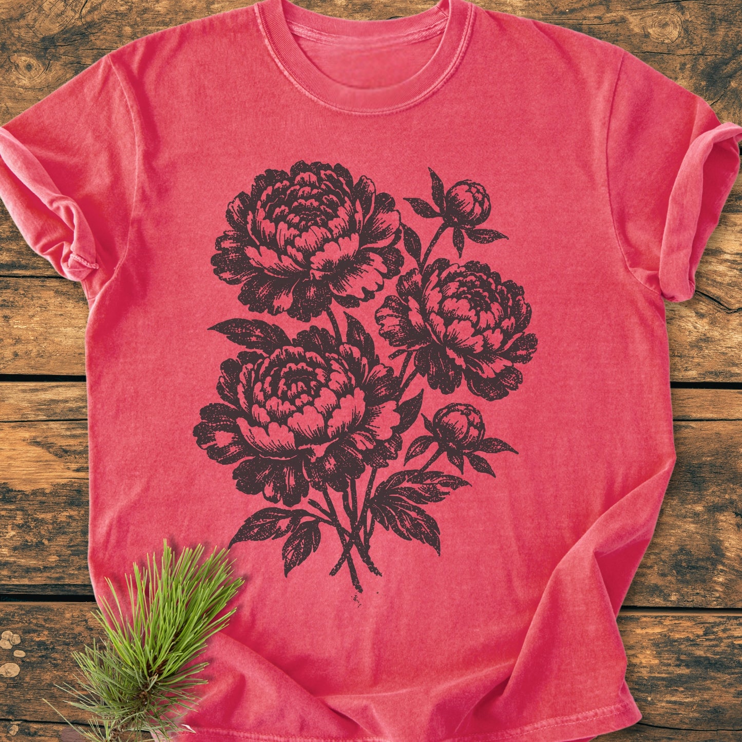 Peony Bouquet - Vintage Heavyweight Tee, in coral-red, features a black floral screen-print with large blossoms. Laid on rustic wood, it showcases the garment's soft, relaxed fit and durable craftsmanship.
