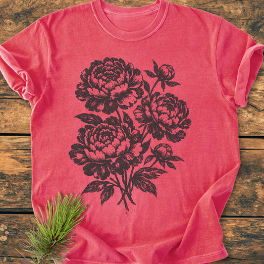 Peony Bouquet - Vintage Heavyweight Tee, in coral-red, features a black floral screen-print with large blossoms. Laid on rustic wood, it showcases the garment's soft, relaxed fit and durable craftsmanship.