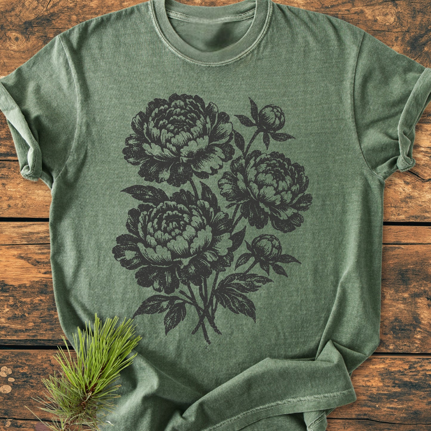 Peony Bouquet - Vintage Heavyweight Tee: Heathered green T-shirt with dark botanical peony illustration, laid on rustic wood with a pine sprig, showcasing the relaxed fit and durable stitching.