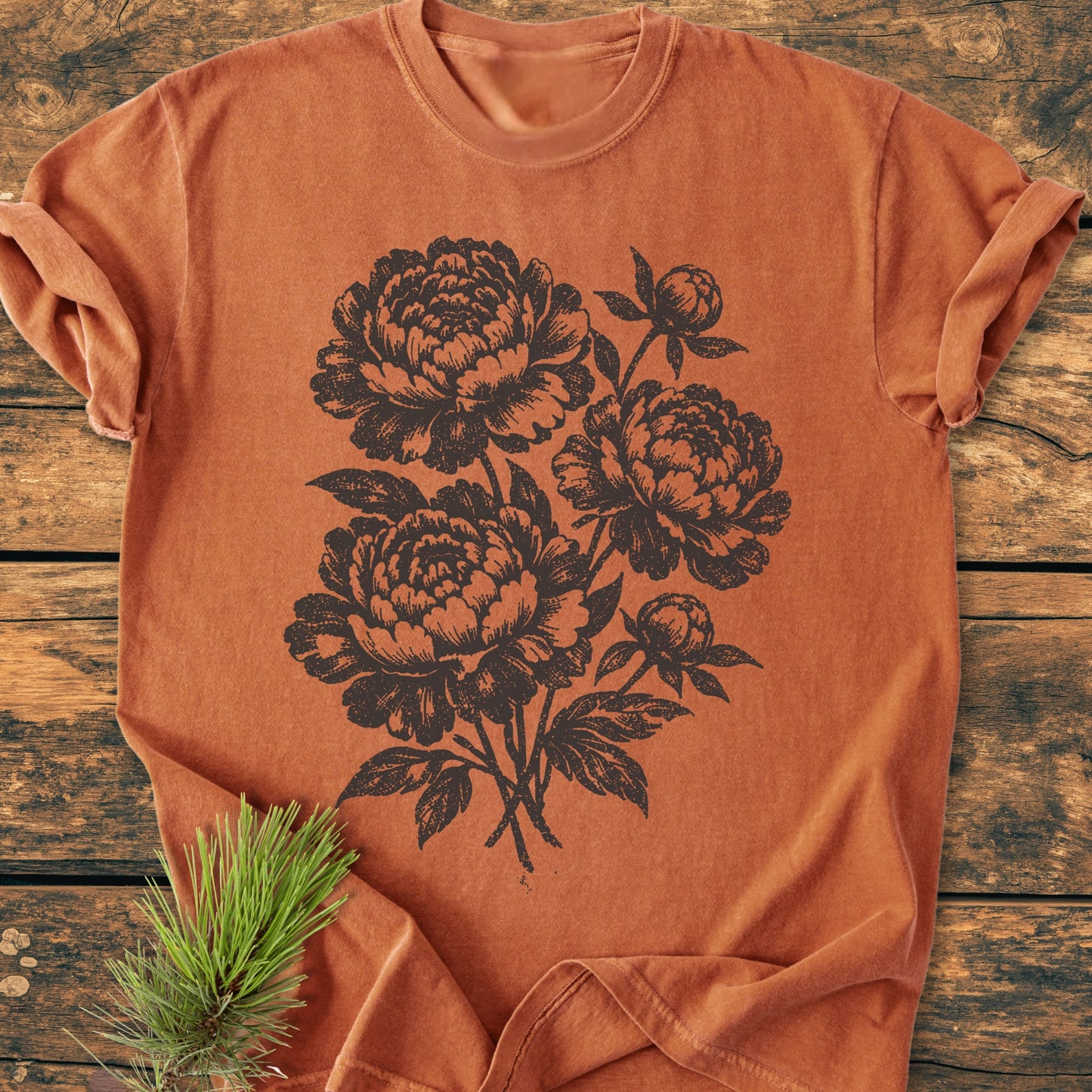 Peony Bouquet - Vintage Heavyweight Tee featuring a detailed botanical peony illustration on a rust-orange surface, laid on a wooden background. Relaxed fit, garment-dyed, made from pre-shrunk 100% ring-spun cotton.