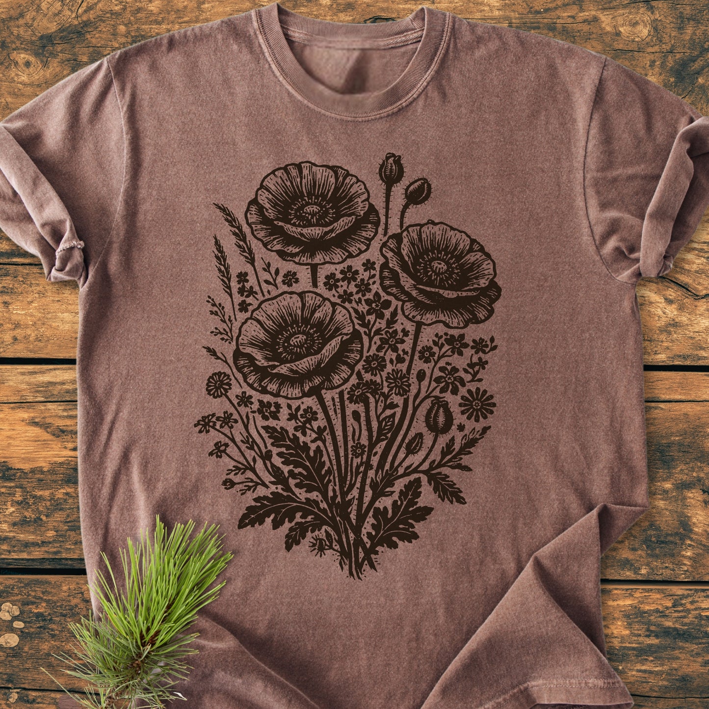 Wildflower Bouquet - Vintage Heavyweight Tee features a detailed poppy bloom illustration on a heather-brown t-shirt, laid flat on wood with a pine sprig, showcasing Comfort Colors' relaxed, durable design.
