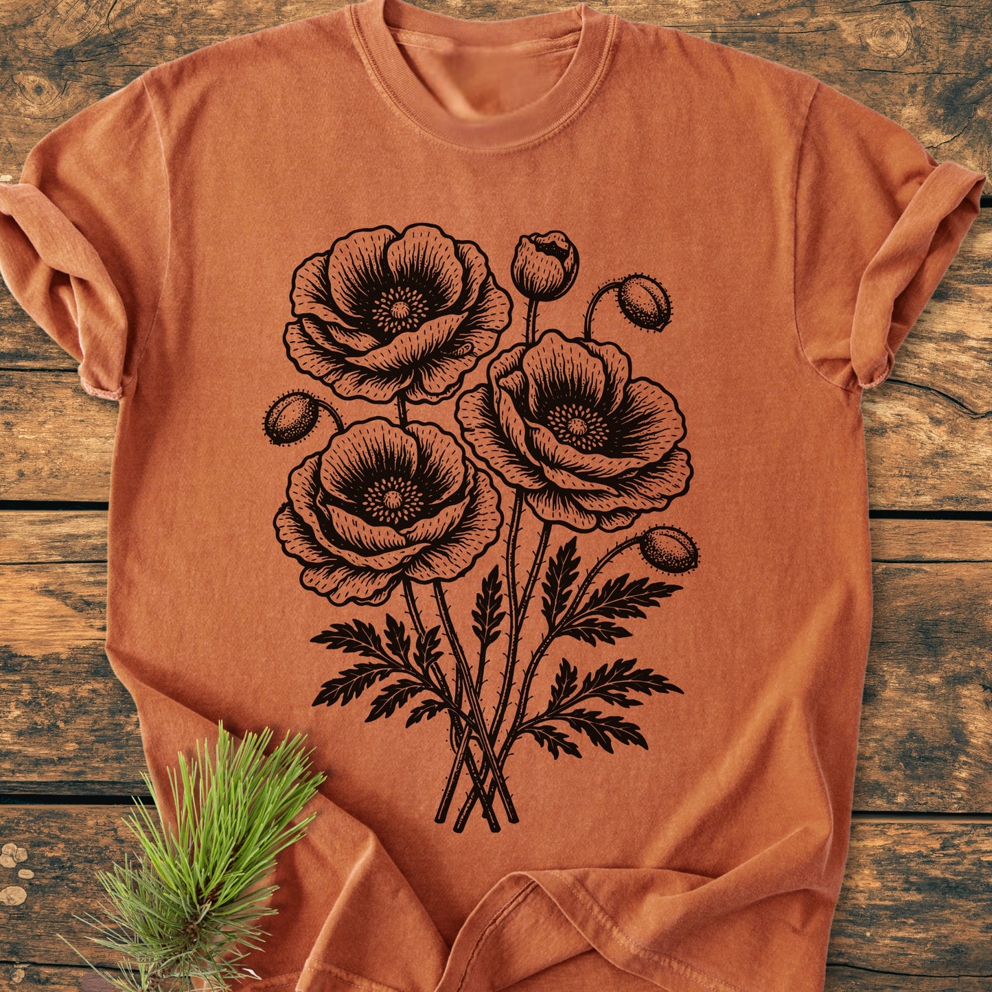 Poppy Bouquet - Vintage Heavyweight Tee features a botanical line drawing of poppies on a rust-orange T-shirt, displayed on a wooden surface.