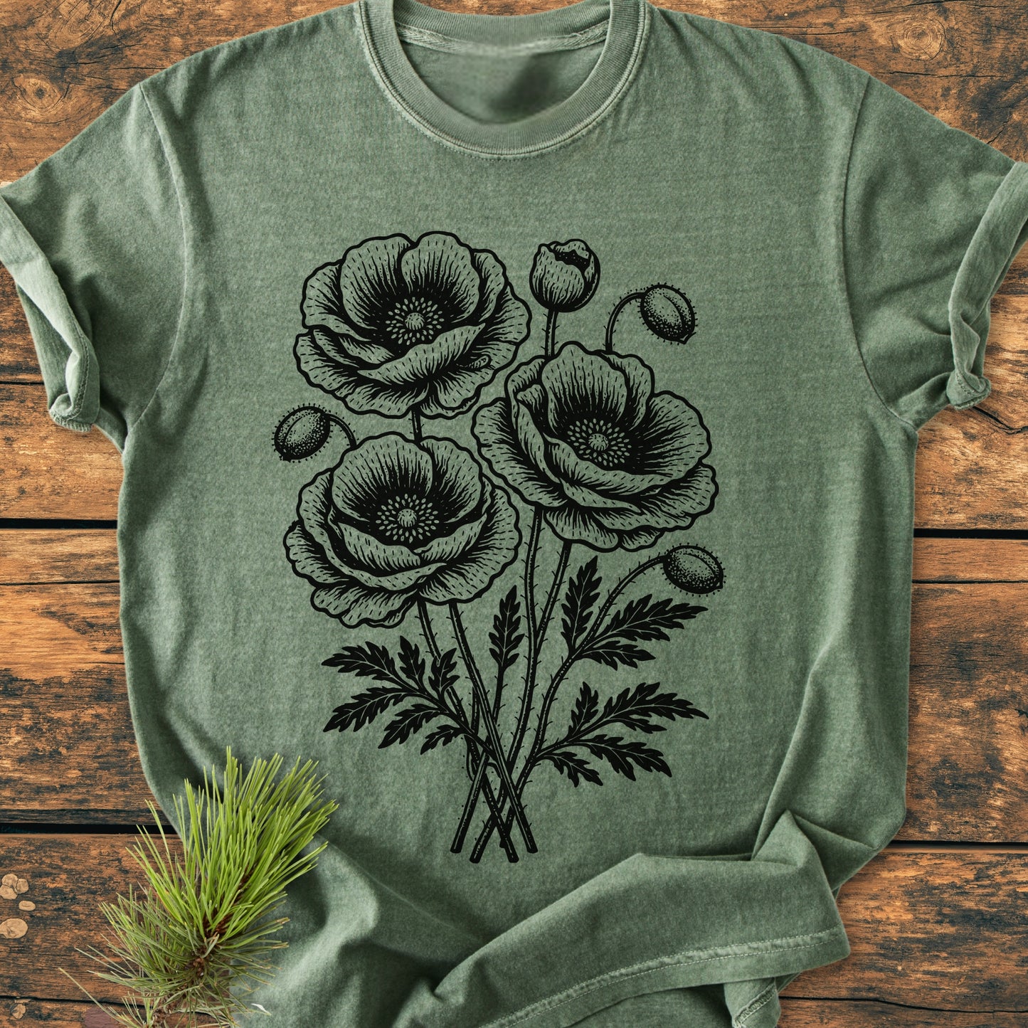 Poppy Bouquet - Vintage Heavyweight Tee featuring a stylized bouquet of poppies in black line art on an olive-green T-shirt, displayed on a rustic surface with a pine twig for styling.