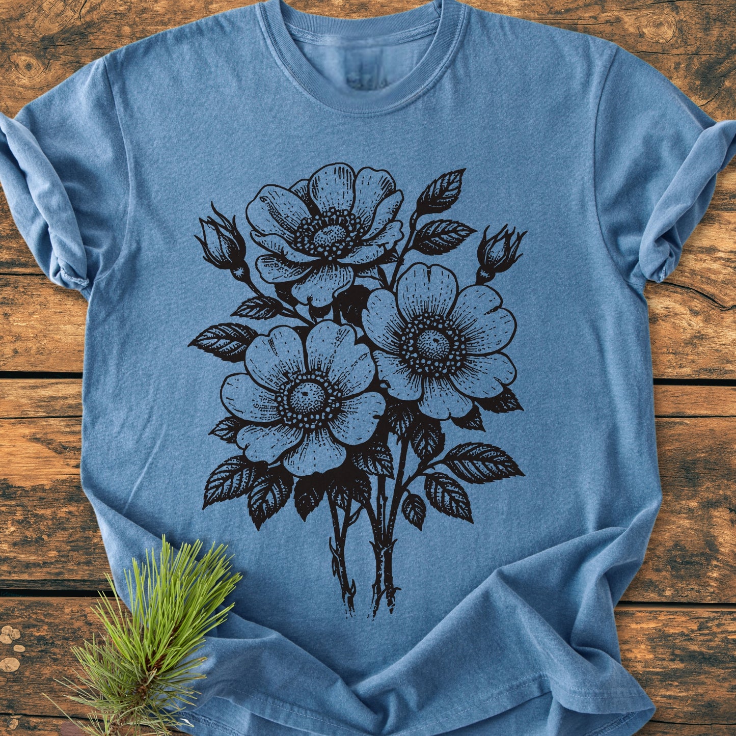 Heather-blue Wild Rose Bouquet - Vintage Heavyweight Tee with black botanical illustration of roses and buds, laid flat on wood. Features relaxed fit, soft-washed fabric, and no side seams for comfort.