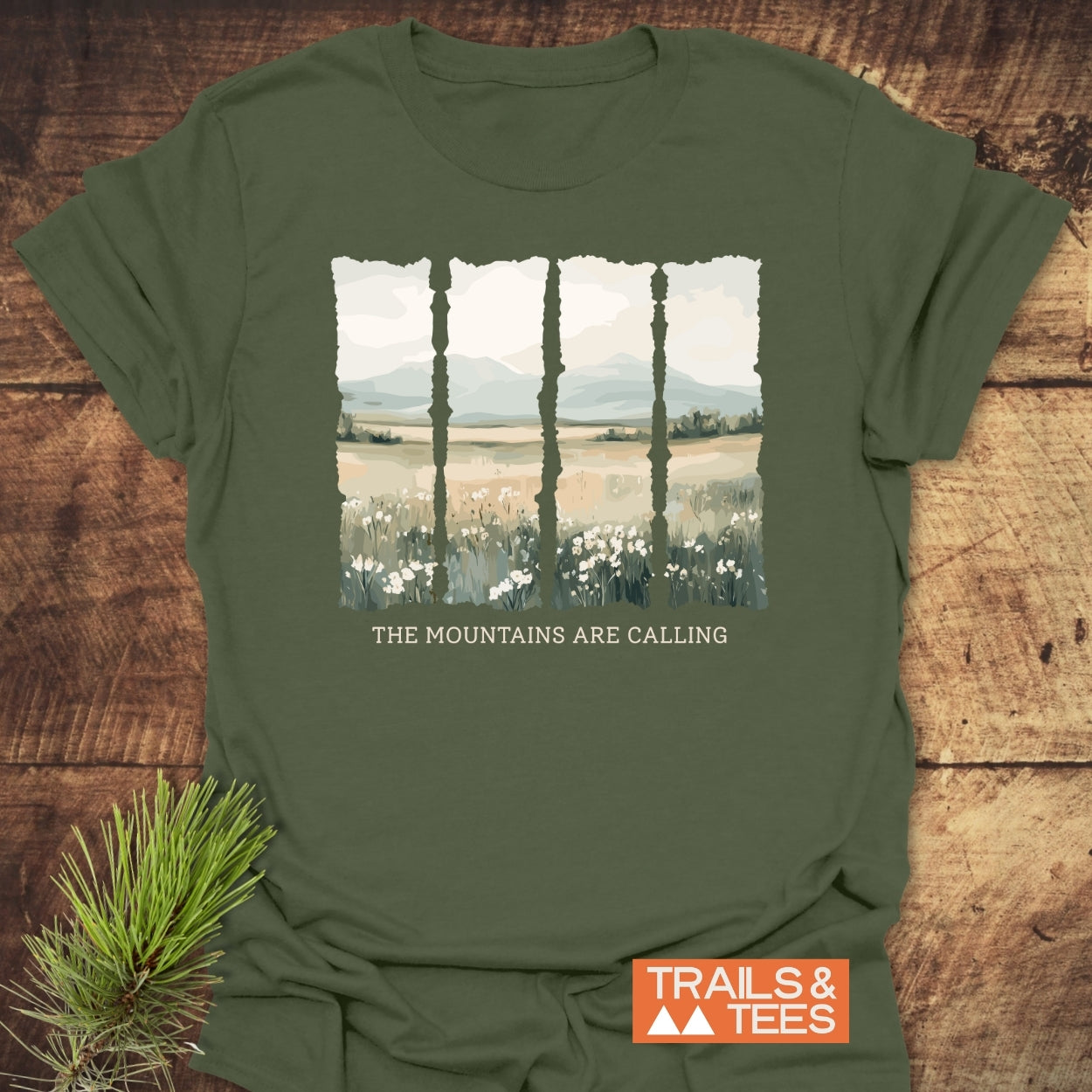 Mountains Are Calling T-Shirt features a four-panel landscape with wildflowers, plains, and mountains, and the phrase “THE MOUNTAINS ARE CALLING” on an olive-green T-shirt by Trails & Tees.