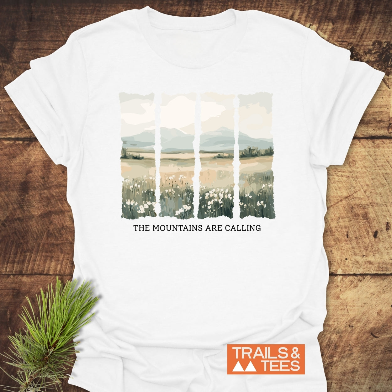 Mountains Are Calling T-Shirt features a four-panel landscape of meadows and mountains with the slogan. Includes Trails & Tees logo, made from lightweight cotton for comfort and durability.