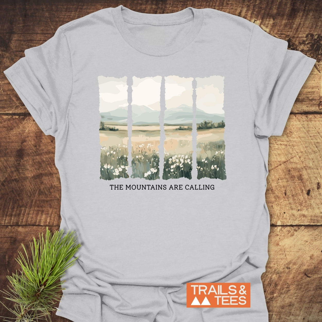 Mountains Are Calling T-Shirt features a four-paneled landscape of wildflowers and mountains. Crafted from soft, ring-spun cotton, it showcases the slogan, ideal for outdoor enthusiasts.