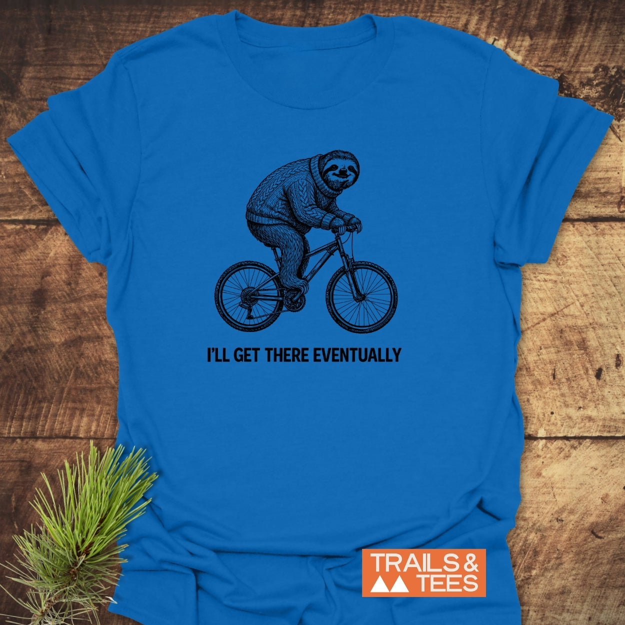 I'll Get There Eventually T-Shirt featuring a cartoon sloth on a bicycle. Crafted from soft ring-spun cotton with durable prints. Includes Trails & Tees logo for adventure enthusiasts.