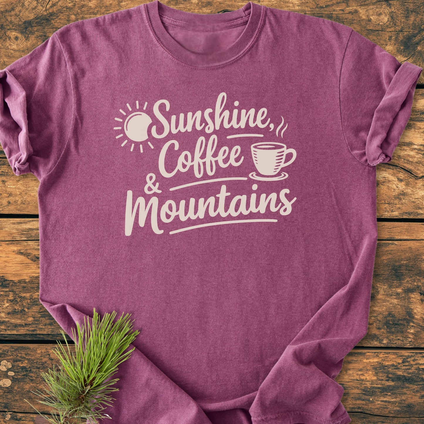 Sunshine, Coffee, Mountains - Vintage Heavyweight Tee displayed flat on wood, featuring a white print with sun and coffee graphics. Includes a pine sprig. Made from soft 100% ring-spun cotton for comfort.
