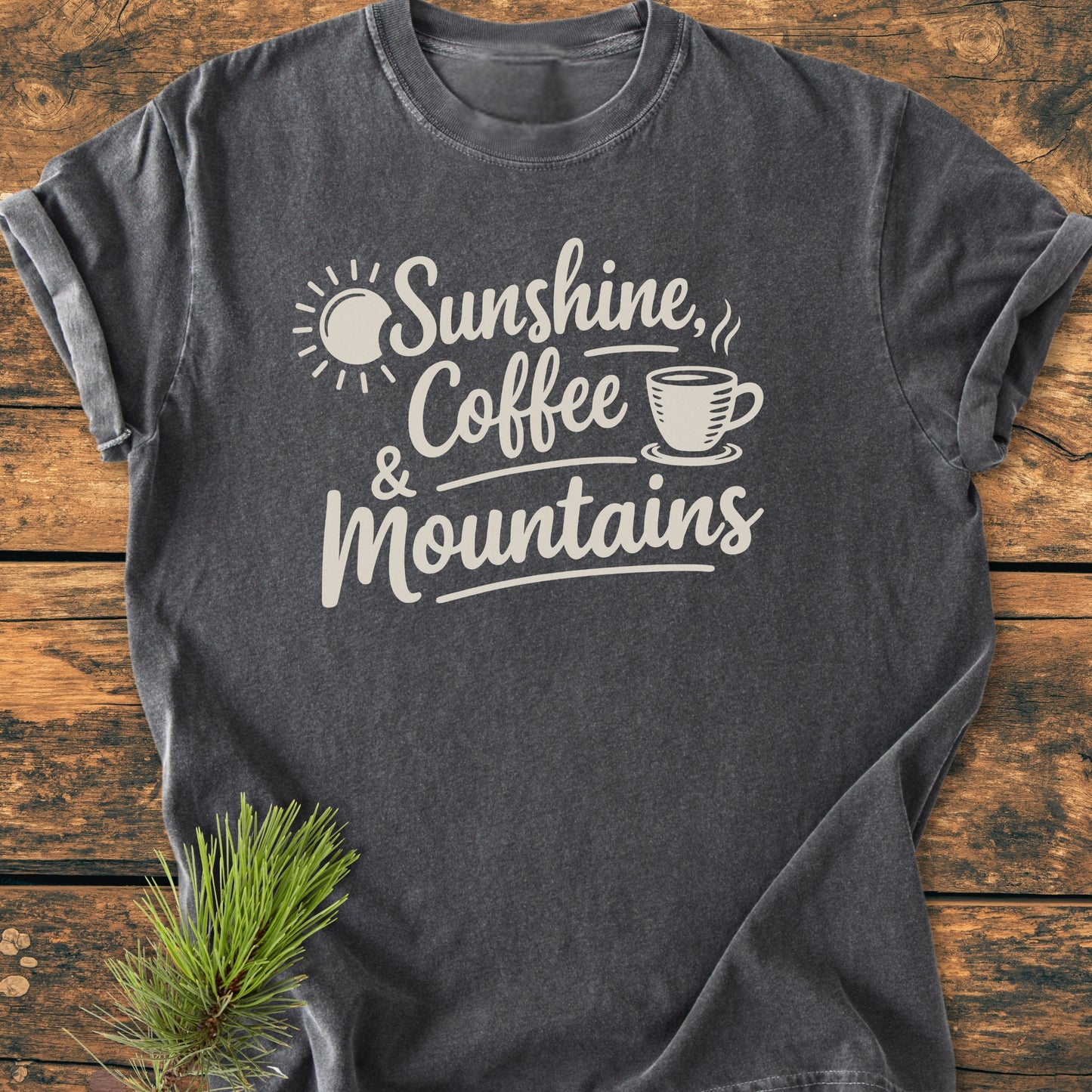 Sunshine, Coffee, Mountains - Vintage Heavyweight Tee featuring rolled sleeves, hand-lettered white graphic, and pine sprig accent, highlighting its relaxed fit and durable construction on a wooden surface.