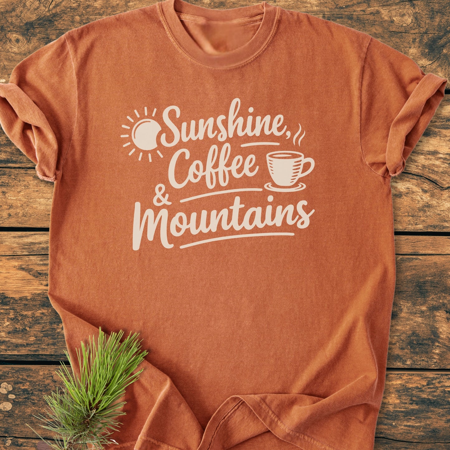 Sunshine, Coffee, Mountains - Vintage Heavyweight Tee featuring a rust-orange hue with white text and graphics. Displayed on wood, with a pine sprig accent. Cozy, relaxed fit, 100% ring-spun cotton.