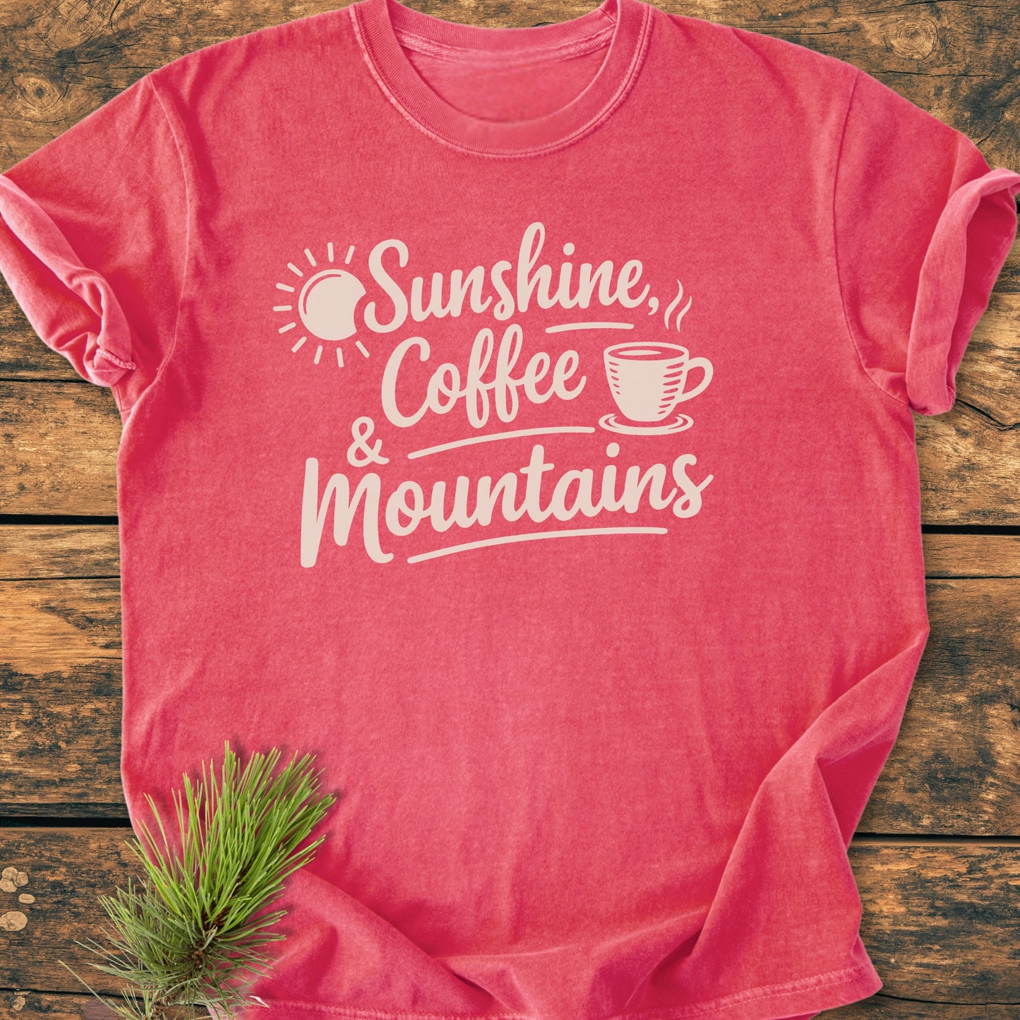 Sunshine, Coffee, Mountains - Vintage Heavyweight Tee displayed flat with white lettering and simple illustrations on a coral-pink background, complemented by a pine branch for a rustic feel.