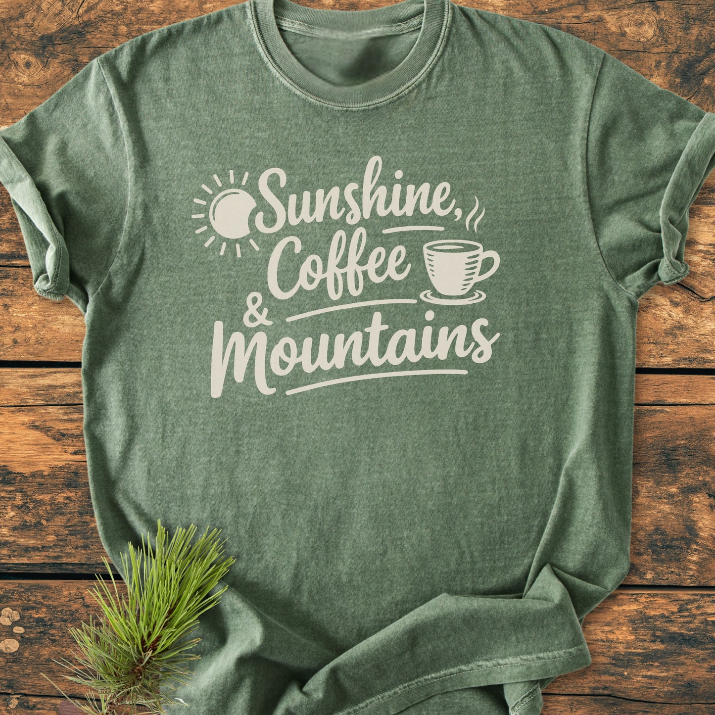 Sunshine, Coffee, Mountains - Vintage Heavyweight Tee showcases a serene graphic with sun, text, and coffee icon on a heather-green T-shirt, complemented by a pine bough for an outdoorsy feel.
