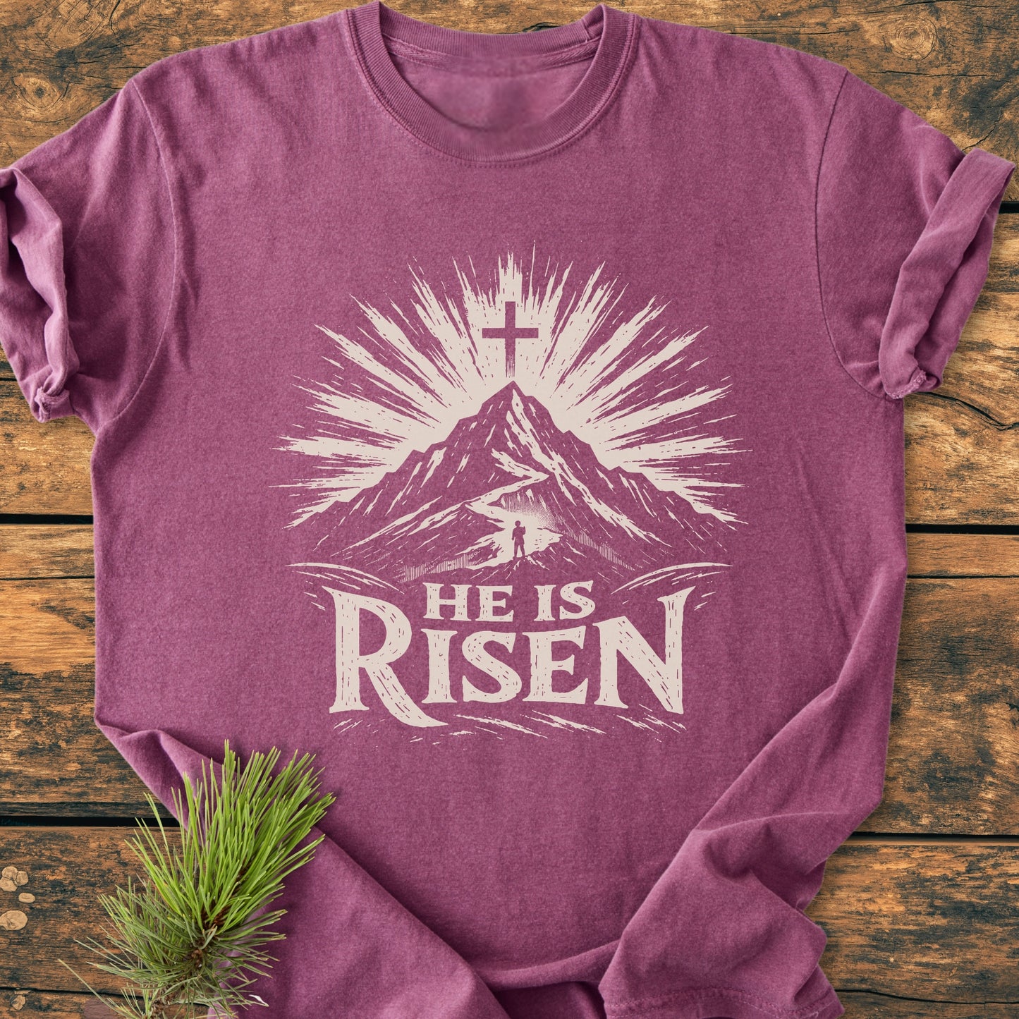 He Is Risen - Vintage Wash Tee: A magenta-tone T-shirt featuring a mountain graphic with sunburst and cross, plus “HE IS RISEN” text, exemplifying comfort with soft, durable, ring-spun cotton.
