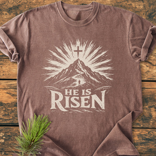He Is Risen - Vintage Wash Tee features a mountain and rising-sun motif with a cross. Made from soft, pre-shrunk 100% ring-spun cotton, it offers a relaxed fit and durable construction.