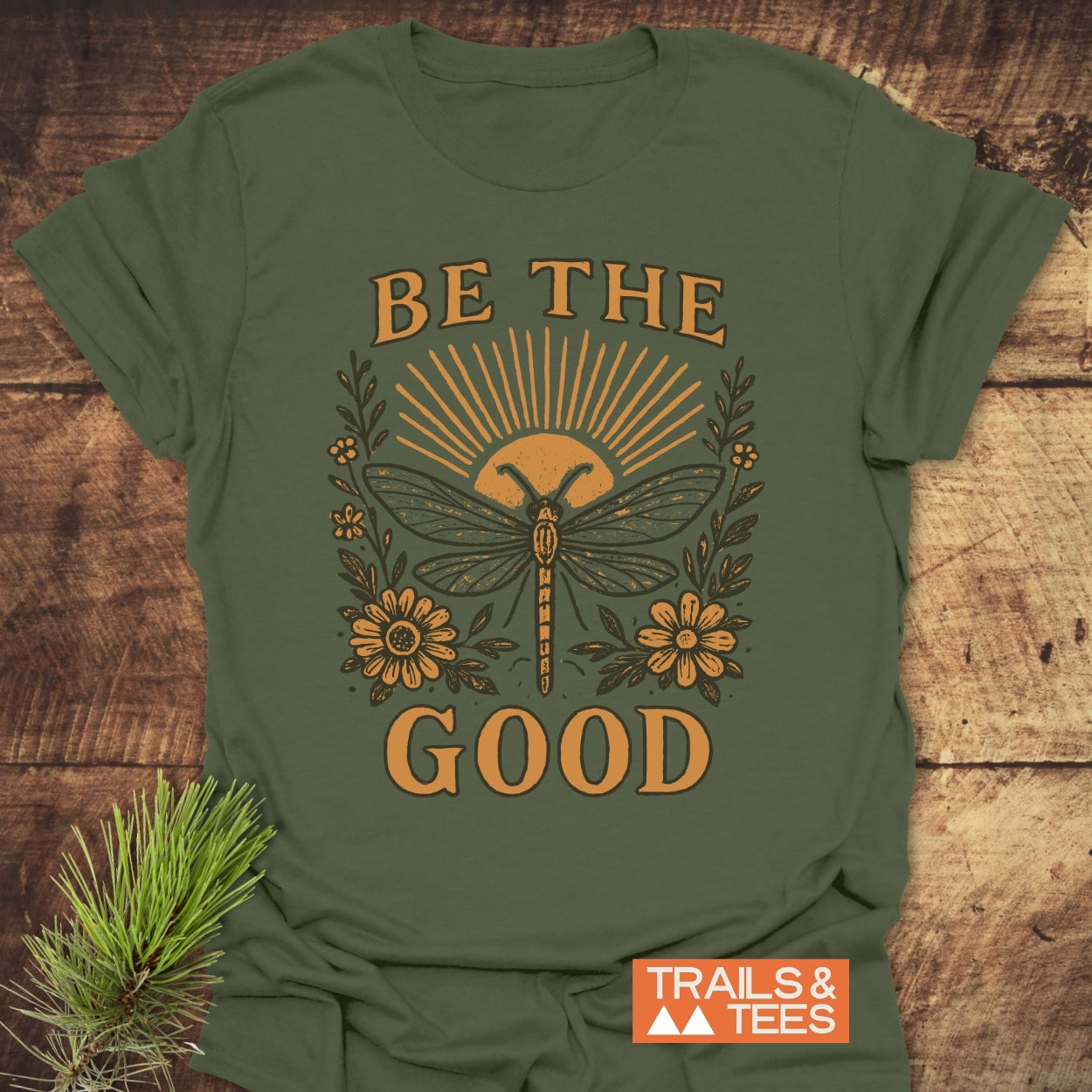 Be The Good T-Shirt featuring a sunburst and dragonfly design with floral accents, crafted from soft ring-spun cotton for comfort, ideal for outdoor adventures and everyday wear.