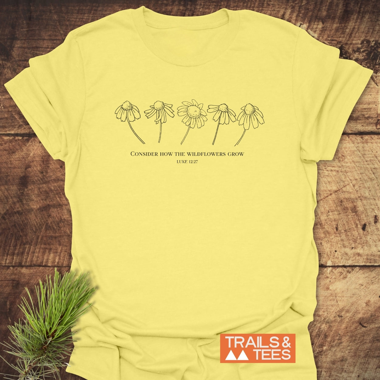 Consider How The Wildflowers Grow T-Shirt featuring line-drawings of wildflowers and biblical quote on soft, ring-spun cotton; includes Trails & Tees logo, emphasizing outdoor adventure and sustainability.