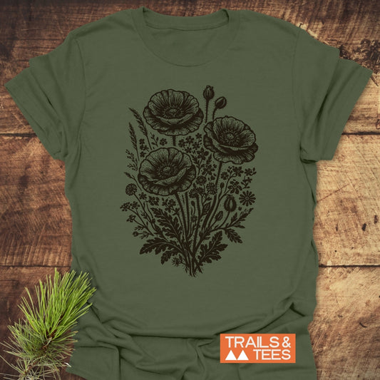 Wildflower Bouquet T-Shirt on rustic wood, featuring a black vintage botanical illustration of poppy blooms and wildflowers, with an orange TRAILS & TEES label nearby.