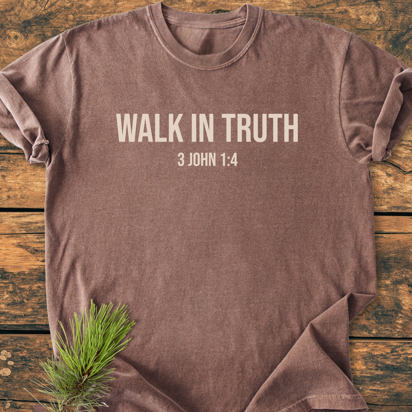 Walk In Truth - Vintage Wash Tee displayed on a wooden surface, featuring rolled sleeves and WALK IN TRUTH with 3 JOHN 1:4 printed. A pine sprig accents the garment's cozy appeal.