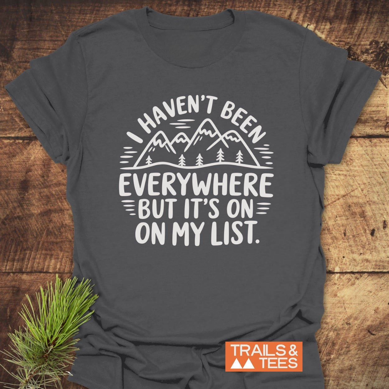 On My List T-Shirt features a white line-drawing of mountains and trees with an adventurous quote, set on soft charcoal-gray fabric, ideal for outdoor enthusiasts.