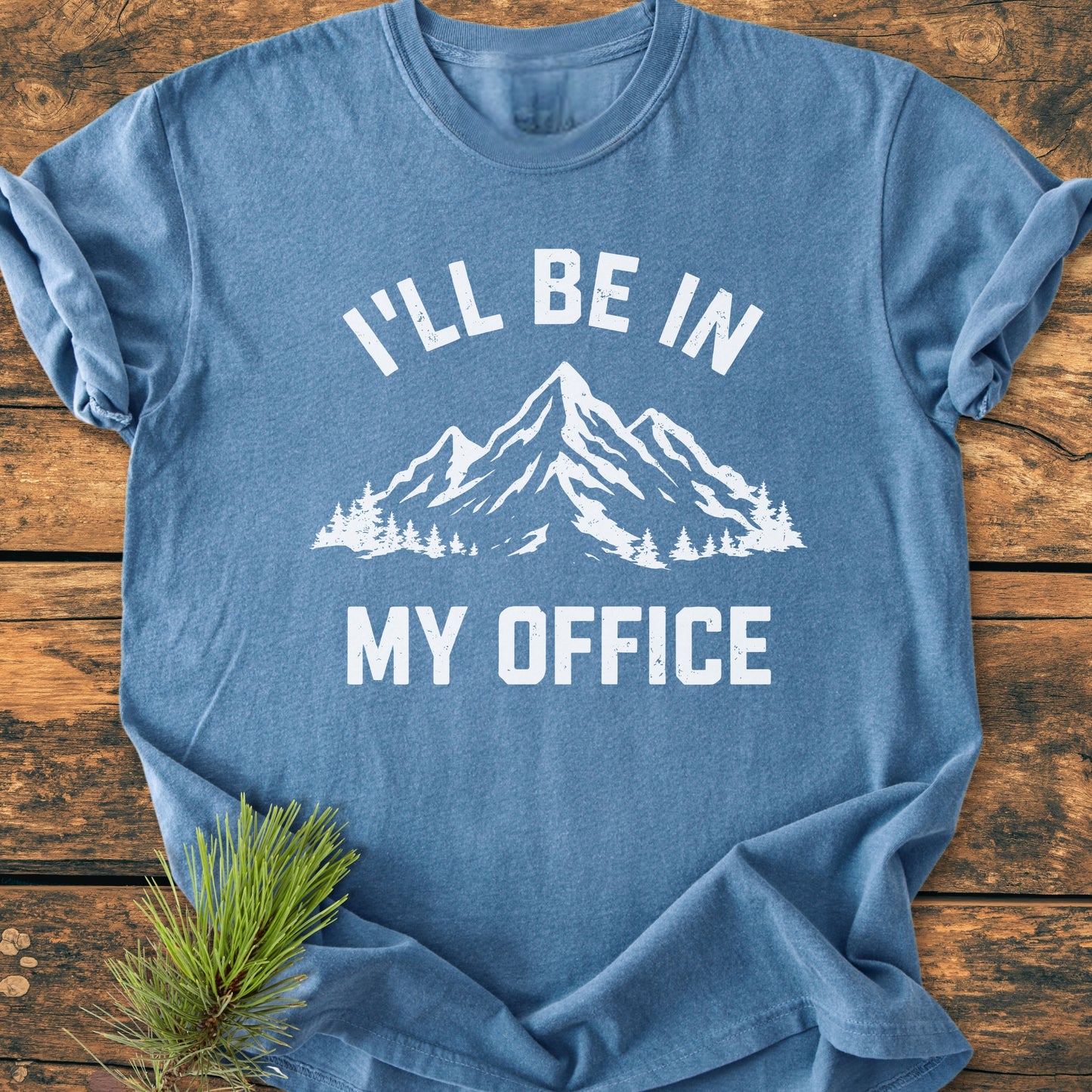 I'll Be In My Office - Vintage Wash Tee with mountain graphics on chest, flat-laid on wood surface, showcasing its relaxed fit and durable stitching, made from soft-washed, 100% ring-spun cotton.