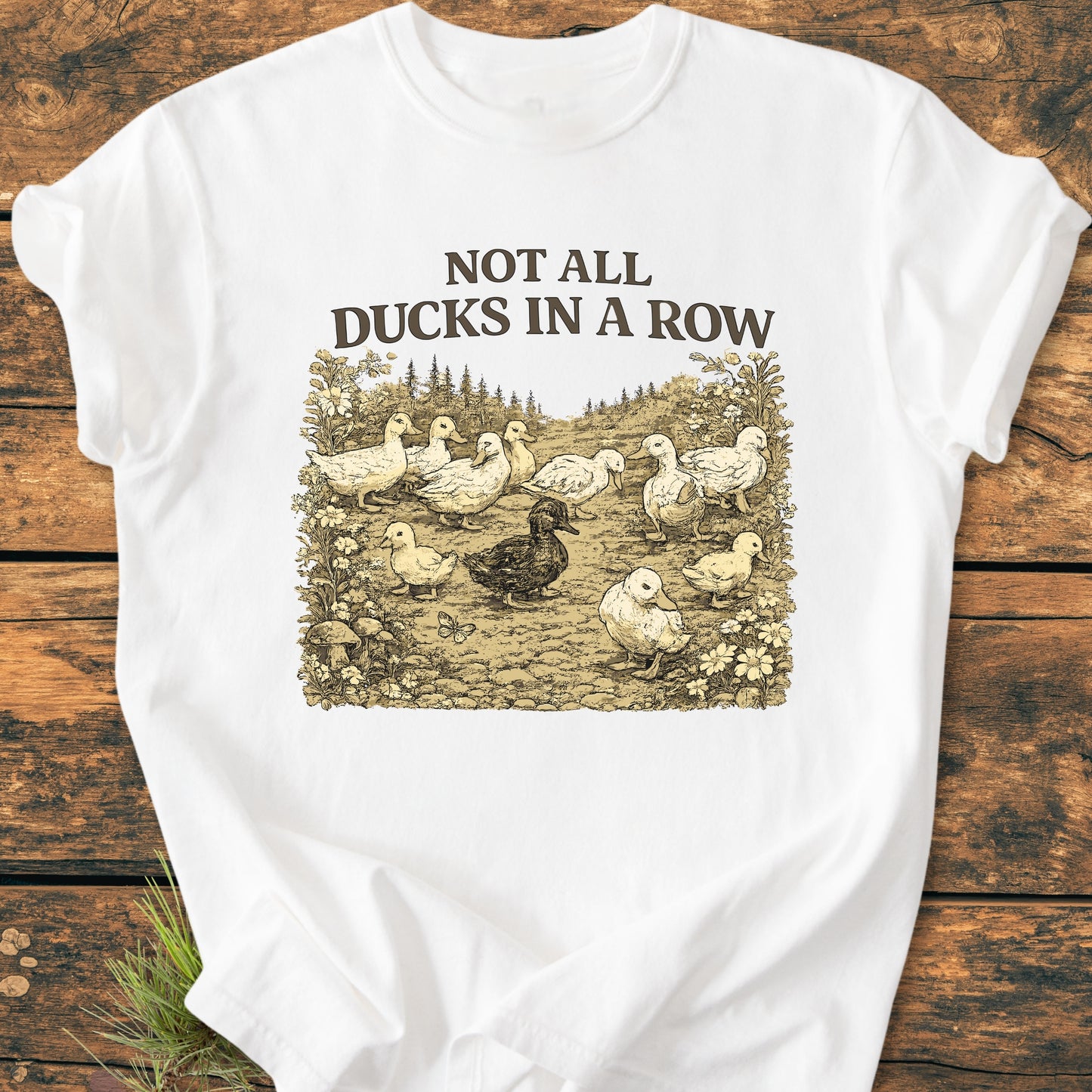 Not All Ducks In A Row - Vintage Wash Tee features a vintage duck illustration with the phrase above, laid on a wooden surface, showcasing its relaxed fit and durable, soft-washed fabric.