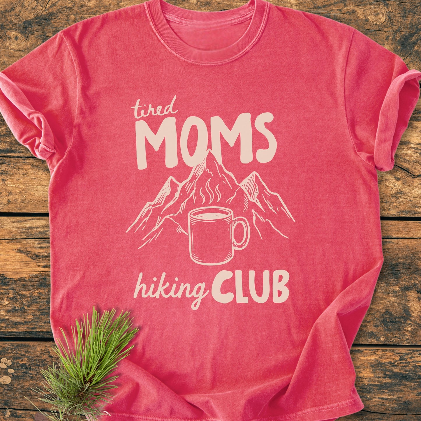 Tired Moms Hiking Club - Vintage Heavyweight Tee featuring a coffee mug and mountains graphic, laid flat with a pine sprig. Made from soft, durable, pre-shrunk 100% ring-spun cotton for comfort.