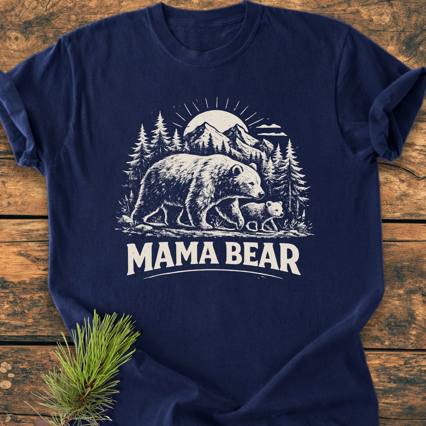 Mama Bear - Vintage Heavyweight Tee featuring a white graphic of a mother bear and cub against a mountain scene, laid on wood with a pine sprig, highlighting its relaxed fit and soft-washed cotton texture.