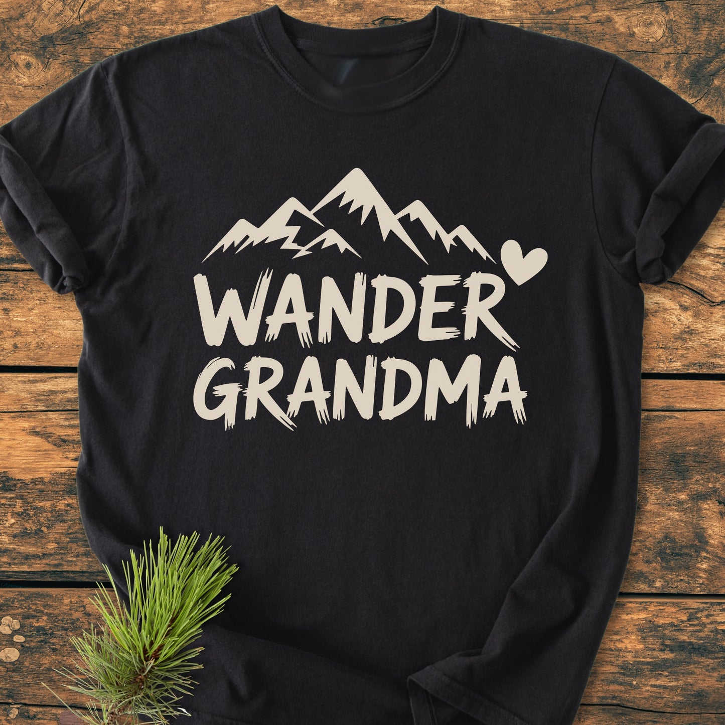 Wander Grandma - Vintage Heavyweight Tee features a black T-shirt with an off-white mountain silhouette and heart design, laid flat on wood, highlighting its relaxed fit and durable construction.