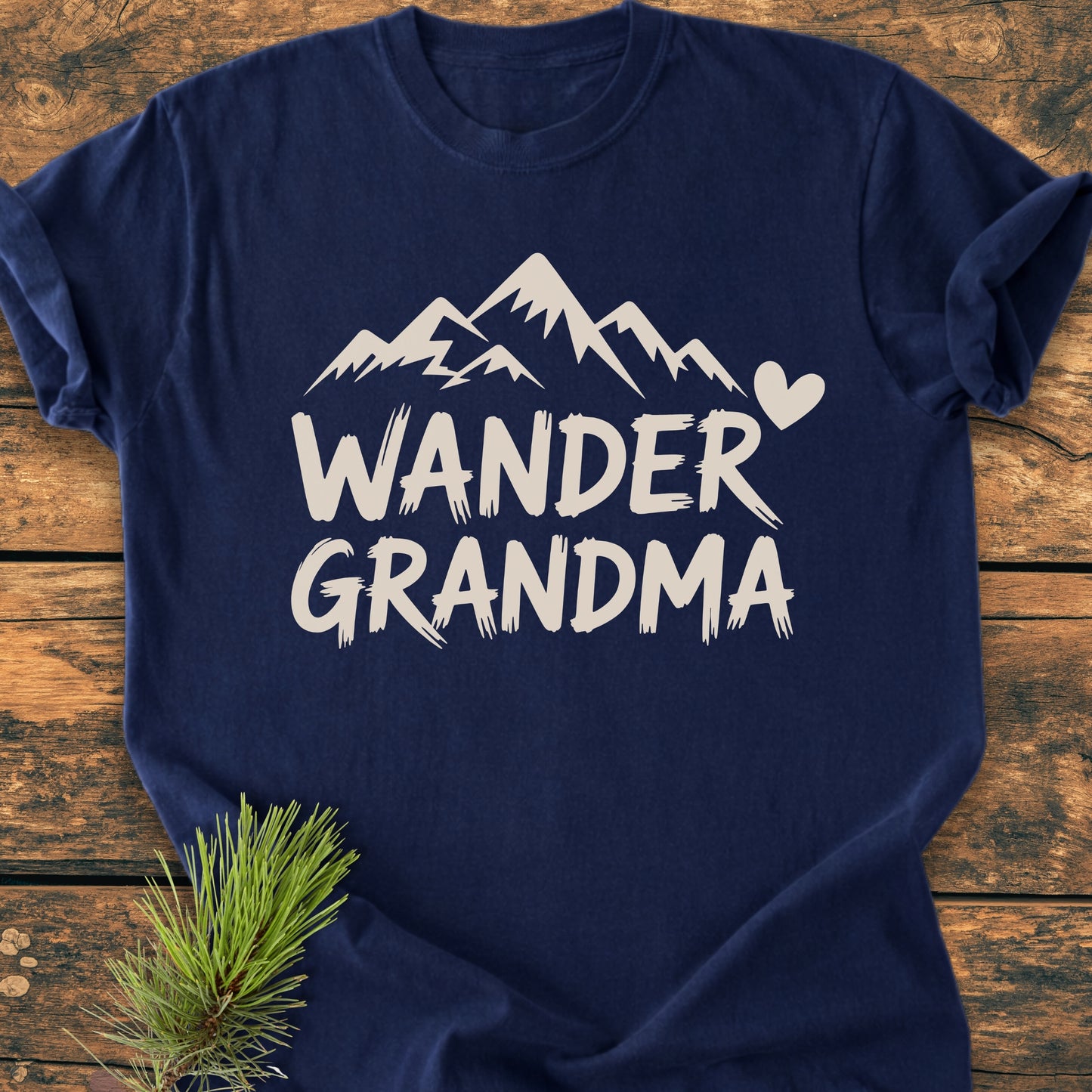 Wander Grandma - Vintage Heavyweight Tee: Navy-blue T-shirt with white mountain range and heart print, laid on wood with pine sprig, showcasing its relaxed fit and durable stitching.