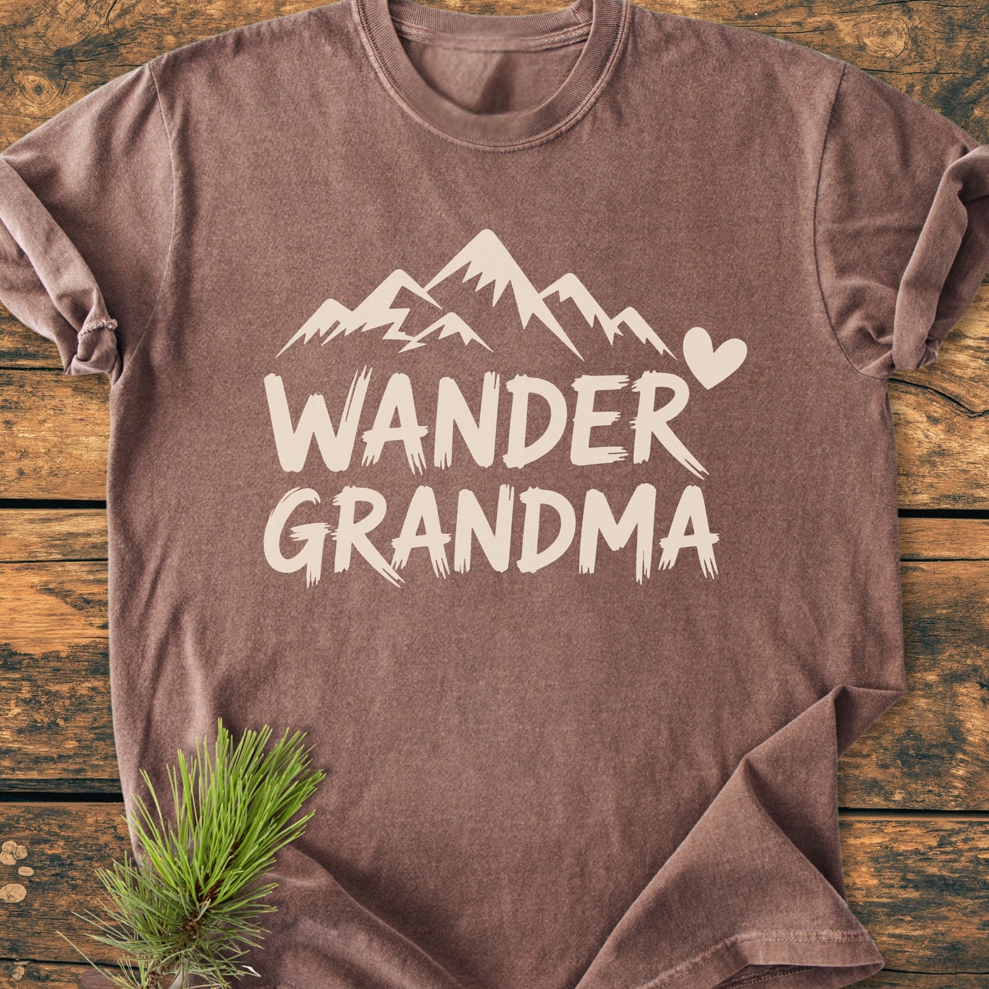 Heather-brown Wander Grandma - Vintage Heavyweight Tee with cream mountain graphic and heart, laid flat on wood. Features soft, durable, 100% ring-spun cotton. Includes pine sprig accent.
