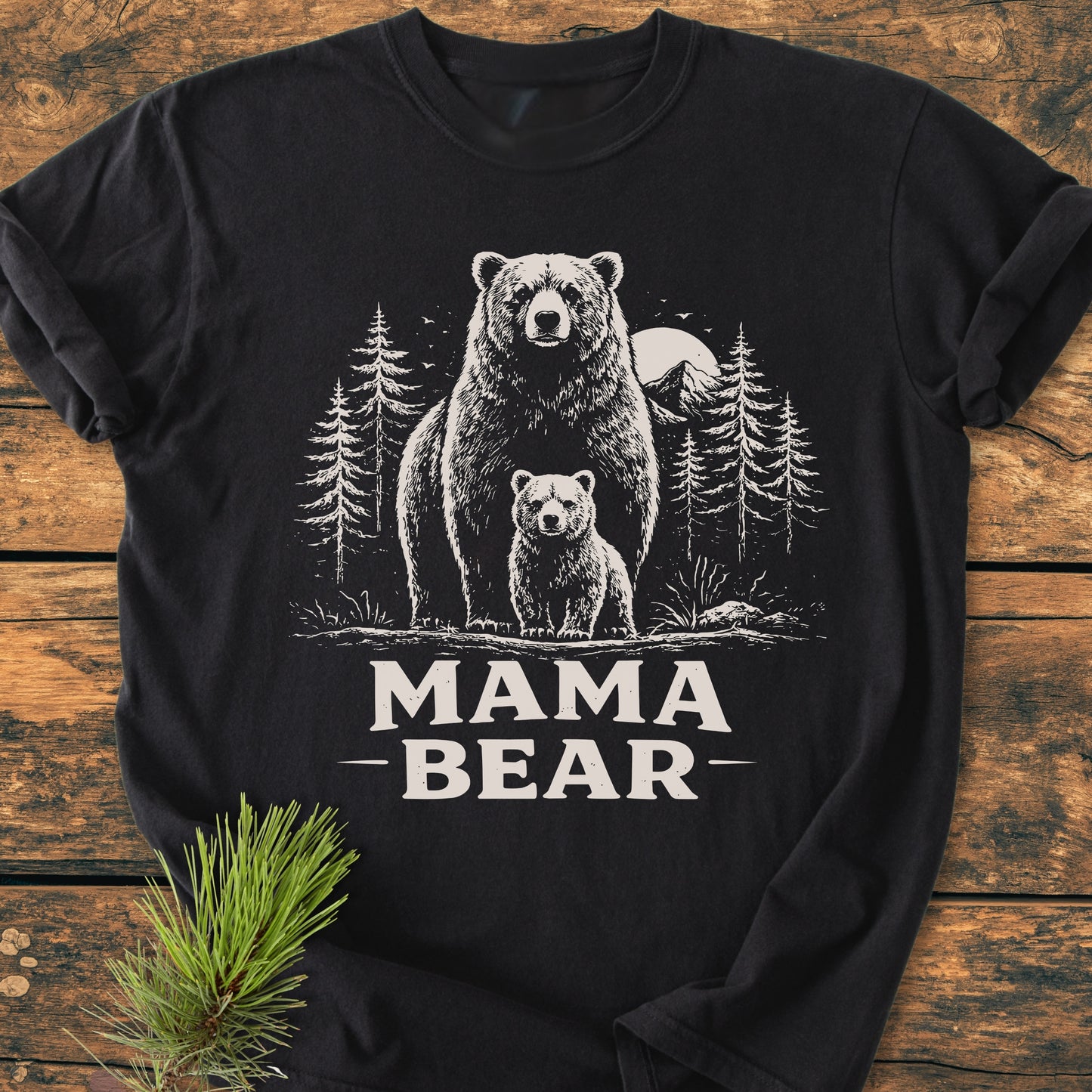Mama Bear - Vintage Heavyweight Tee features a bear and cub design with mountain backdrop, printed on a black Comfort Colors 1717 T-shirt, laid on rustic wood with pine sprig.