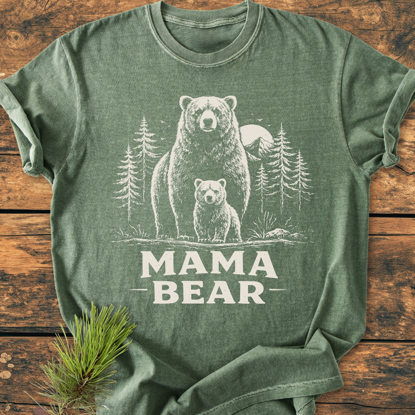 Mama Bear - Vintage Heavyweight Tee in forest-green, featuring a white bear graphic with cub and MAMA BEAR text, laid out on wood with a pine sprig accent, highlighting its cozy, durable design.