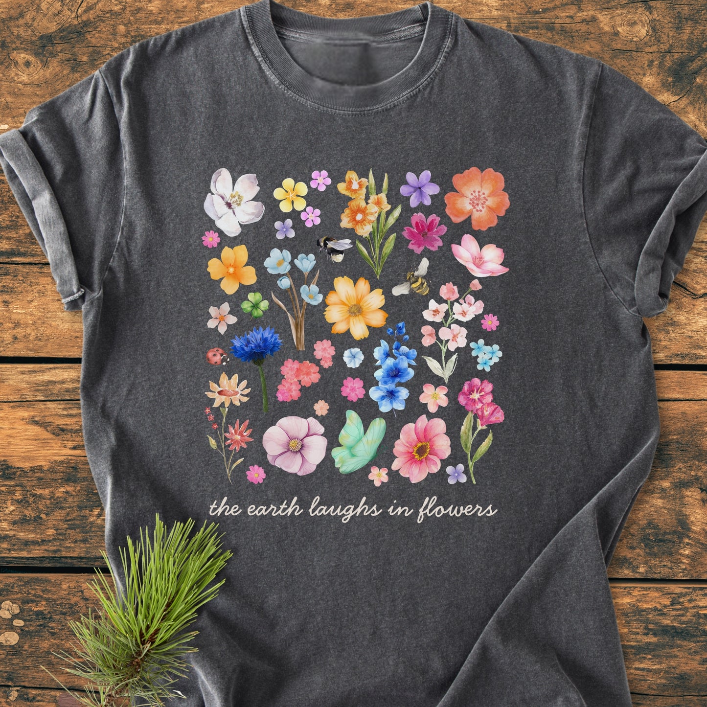 The Earth Laughs In Flowers - Vintage Heavyweight Tee features a vibrant floral grid with bees and a ladybug on a charcoal-gray backdrop, highlighted by the phrase in elegant white script.